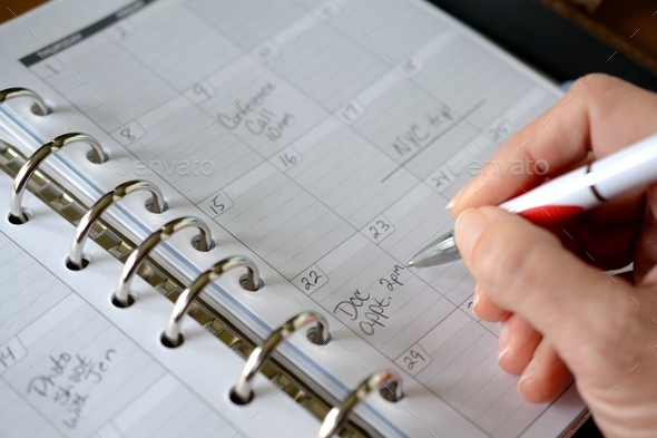 Female making notations of appointments, trips and events on a planner calendar in a binder