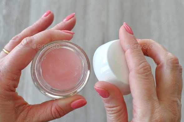 A female woman lady wearing pink fingernail polish opening a jar of pink gel moisturizer cream.