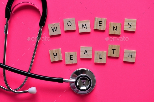 Overhead flat lay of a stethoscope on pink background with words WOMENS HEALTH spelled out in tiles