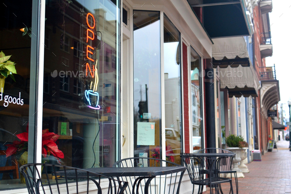 A neon OPEN sign with a steaming mug of coffee in the window of a cafe with outdoor seating