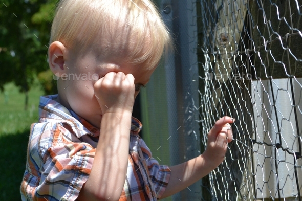 Tired little toddler boy child crying and rubbing his eyes outside.