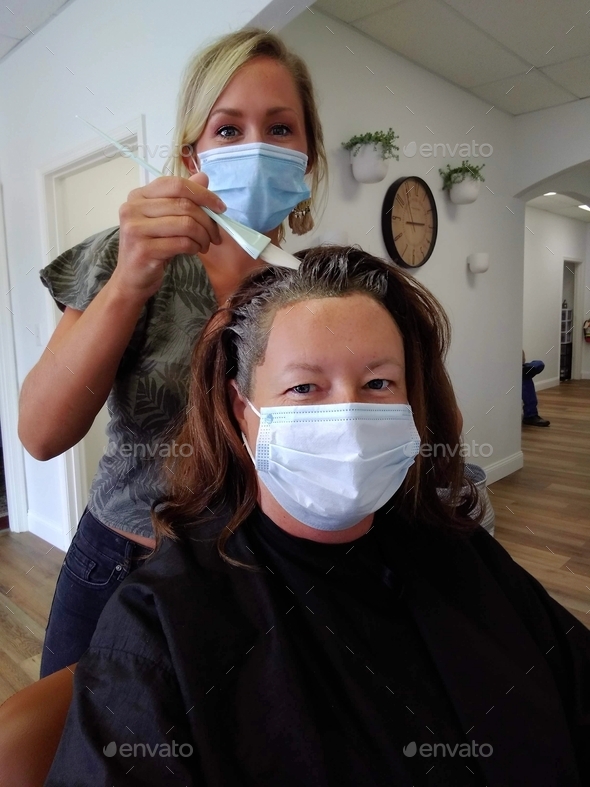 Woman getting her hair colored at a hair salon hairdresser\'s both female women wearing a face mask