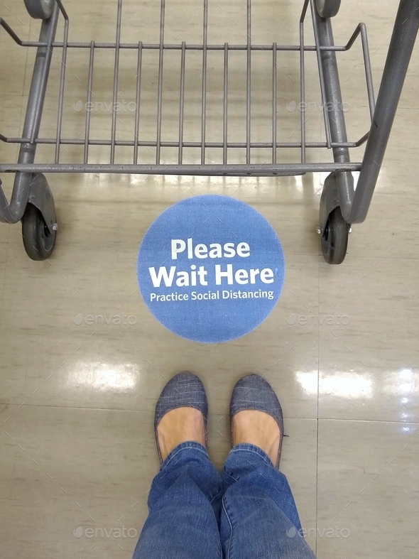  Sign on floor saying, Please Wait Here Practice Social Distancing with woman\'s feet & shopping cart