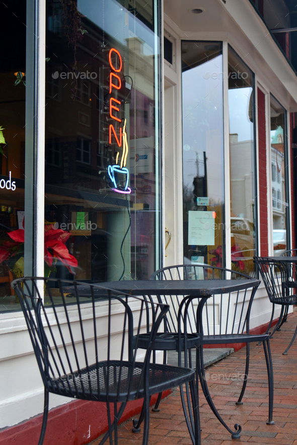 A neon OPEN sign with a steaming mug of coffee in the window of a cafe with outdoor seating