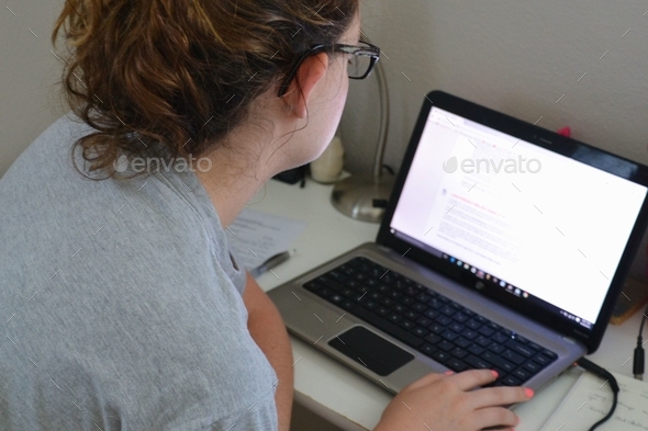 Female student doing her homework on a laptop computer with a messy bun