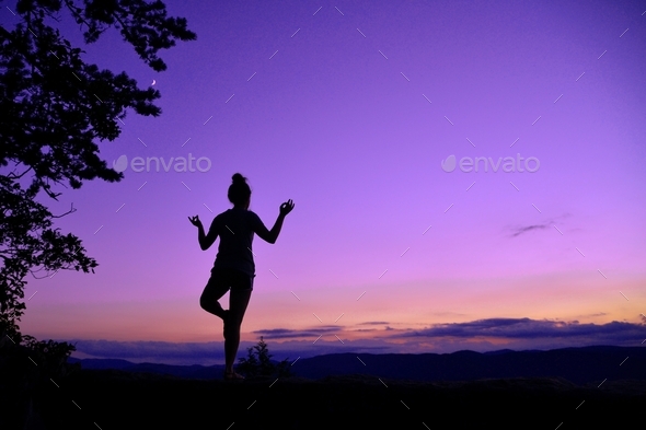 Purple Yoga - female with messy bun doing yoga against a vivid purple pink magenta sunset sky