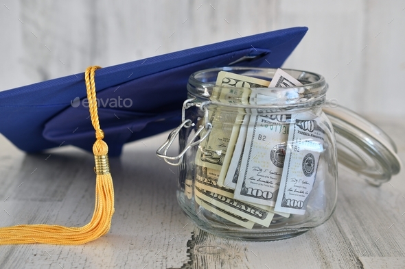 Graduation cap mortarboard with tassel propped on a jar of money cash, concept school loans debt