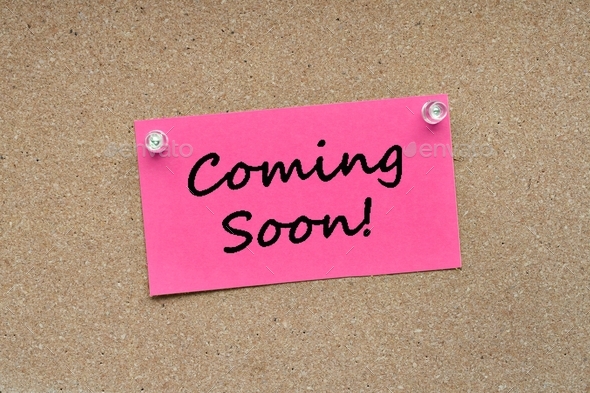 Pink note card pinned with push pins on a corkboard bulletin board with the words Coming Soon!