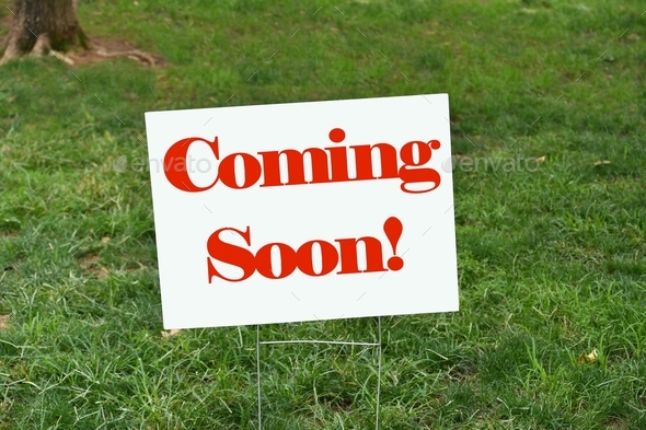 Coming Soon! sign in the grass announcing there will be a new addition in the near future.