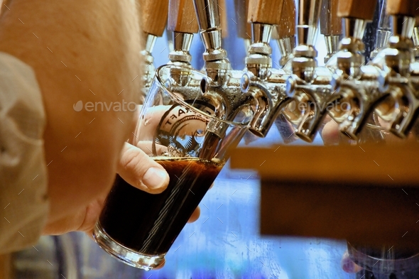 A man filling a glass with a dark beer like a porter or stout from a beer tap.