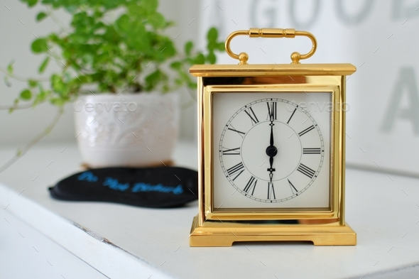 Classic timepiece gold clock with roman numerals setting on a dresser with a Do Not Disturb eye mask