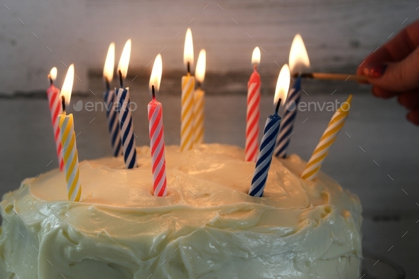 Female hand lighting candles on a birthday cake with a wooden match at a birthday party.