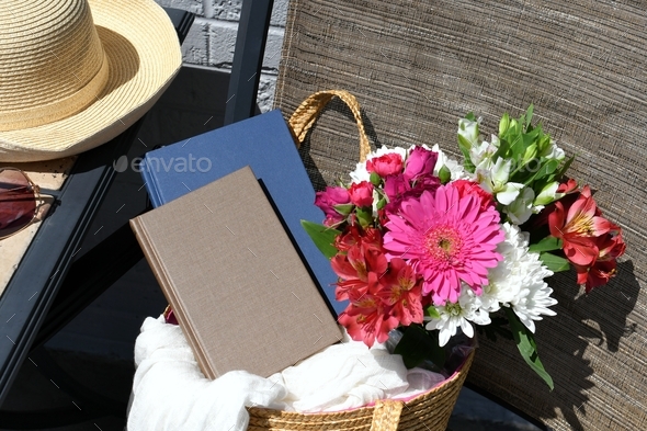 Book cover mock up - plain book in straw tote bag outside with flowers summer hat
