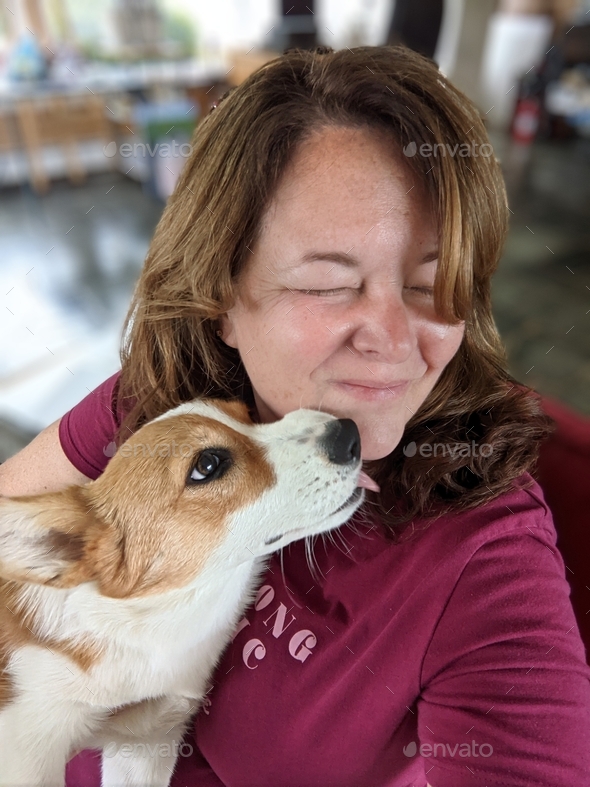Middle aged female woman reacting to getting her face licked by a Corgi puppy dog