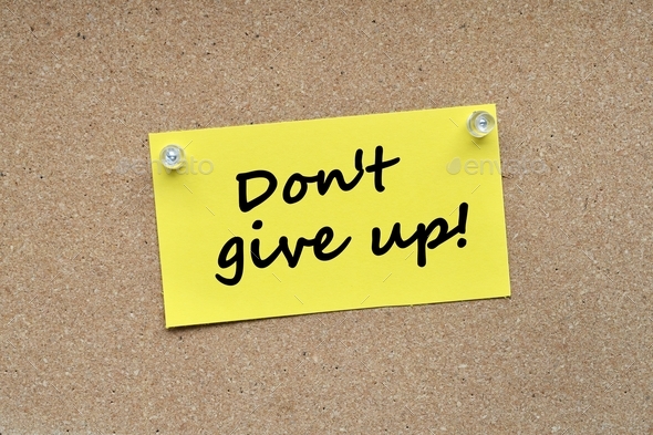 Yellow note card pinned with push pins on a corkboard bulletin board with the words Don\'t Give Up!