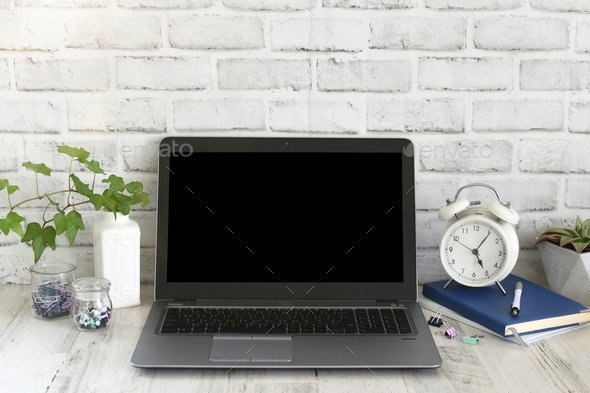 Laptop computer on a desk in a bright minimal modern office with blank black mock up mockup screen