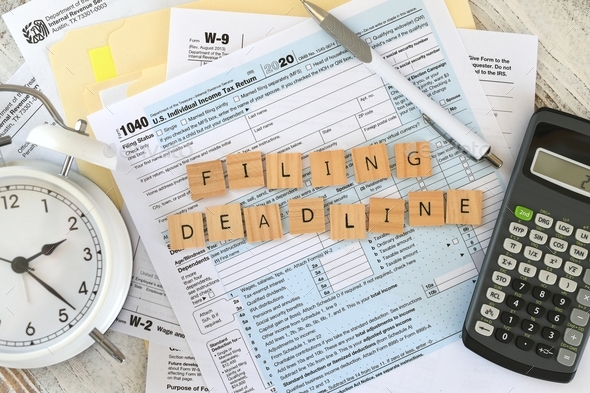 IRS tax forms 1040 words FILING DEADLINE in wooden tiles with calculator W2 W9 April 15 clock