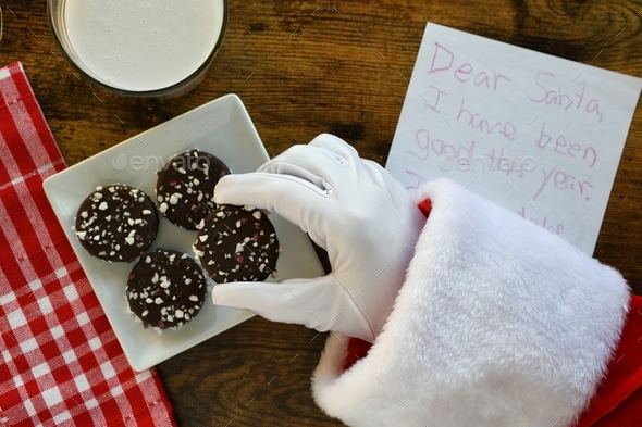 Santa Claus grabbing cookie & milk left out for him with note on Christmas Eve. Overhead flat lay