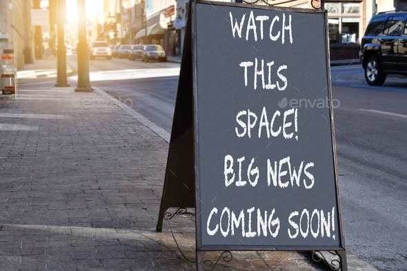 Chalkboard sign on sidewalk proclaiming Watch This Space Big News Coming Soon!