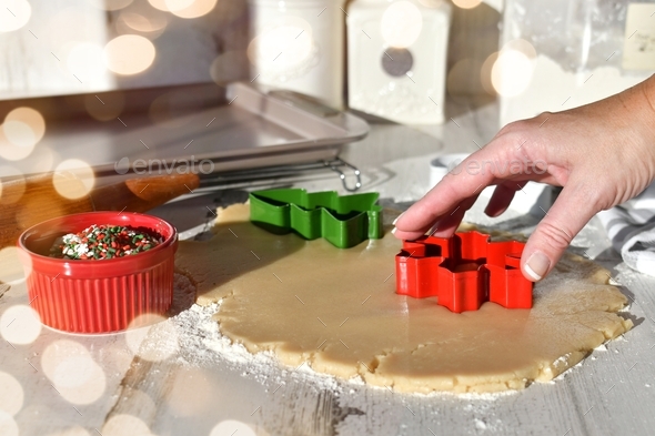 Female making Christmas cookies using red green cookie cutters on rolled out cookie dough