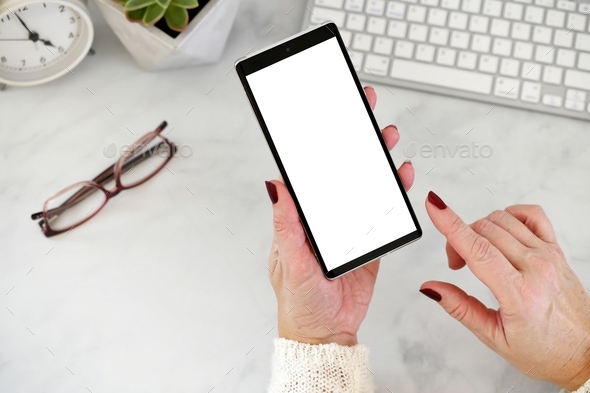 Female holding mobile phone at desk with blank white screen finger posed to click on screen mock up
