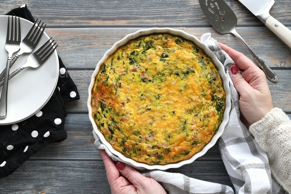 A ham, cheese & spinach quiche. Flat lay of female placing cooked ...