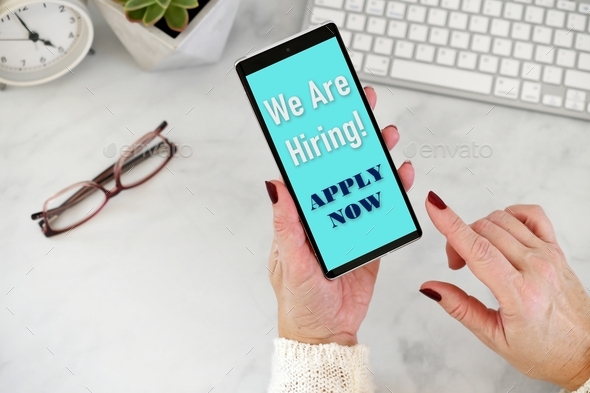 Online Job Search - We are Hiring Apply Now on phone screen with desk in background