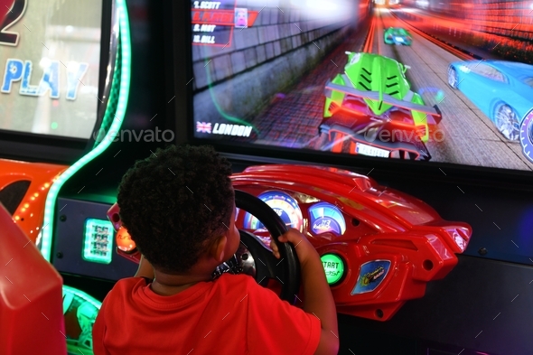 Small African-American boy playing a race car driving game in an arcade.  - Stock Photo - Images