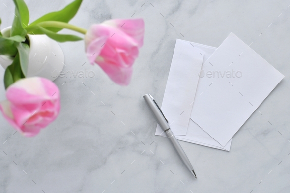 Blank card with envelope pen for mock up on writing desk with pink tulips, minimalist simple