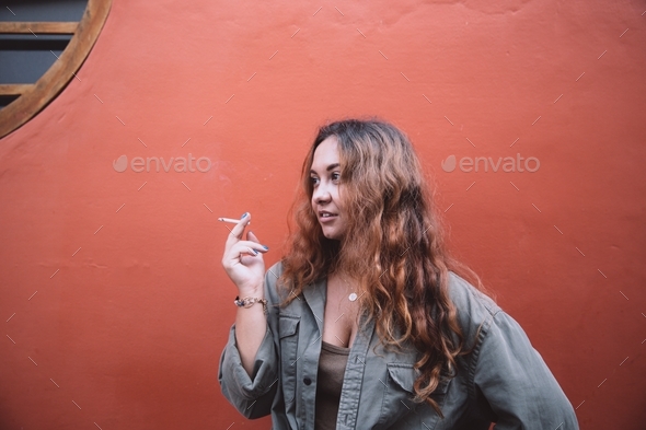 beautiful woman smoking standing by coral bright wall