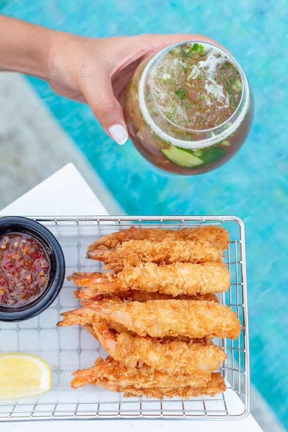 Breaded shrimps with chili sauce, slice of lemon and cocktail in hand served at the swimming pool
