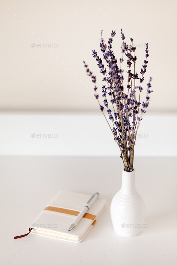 Lavender bouquet in a white vase next to notebook with pen. Interior decoration, minimalism concept.