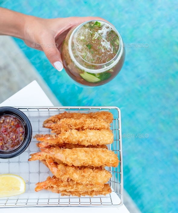 Breaded shrimps with chili sauce, slice of lemon and cocktail in hand served at the swimming pool