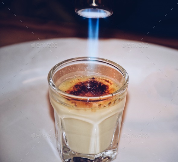 Burning the sugar layer of creme brûlée with a torch Stock Photo by