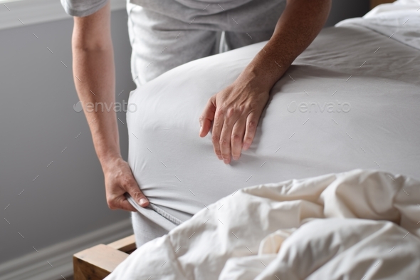 Woman’s hands putting on fitted bed sheet on a mattress while changing bed sheets