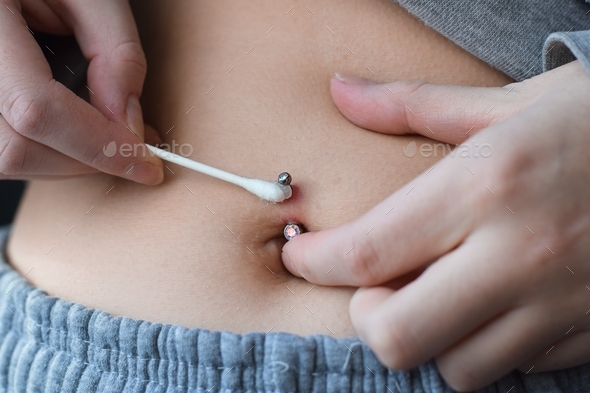 Young girl applying antibiotic cream with cotton swab on infected belly button piercing
