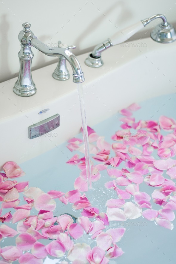 Modern white freestanding bathtub with pink rose petals filling with running water Stock Photo