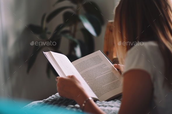 Young teenage girl laying on her bed reading a book