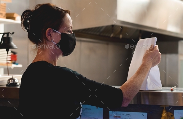 Female restaurant server employee in a face mask is taking care of customer’s take out order