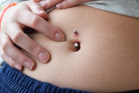 Young teenage girl looking at the redness on her belly button piercing possibly infected