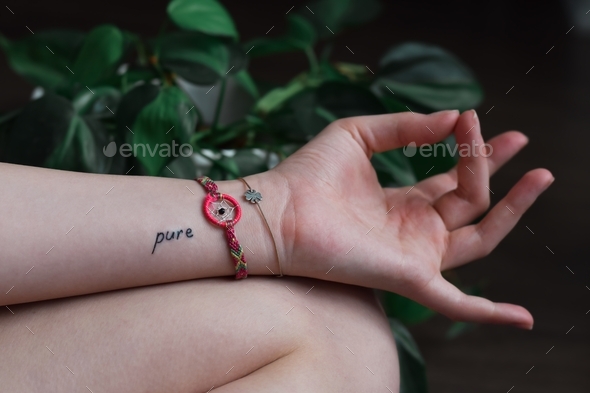 Closeup of young girl hand in Akash or Shuni Mudra meditation pose and word Pure tattoo on wrist