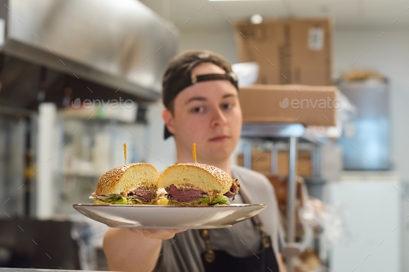 Restaurant kitchen employee holding plate with sandwich food order ready