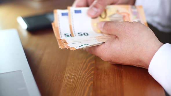 Man Counting Euro Banknotes Sitting at the Table
