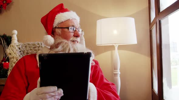 Santa claus looking through window while using digital tablet alt