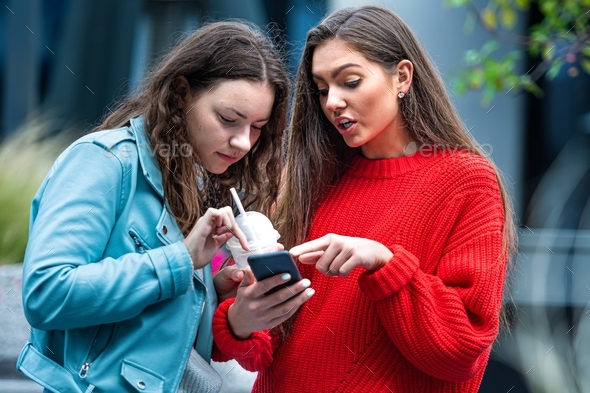 two girlfriends use a smartphone, laugh and talk, fun together, new normal tech concept