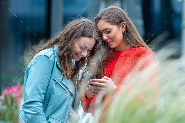 two girlfriends use a smartphone, laugh and talk, fun together, new normal tech concept