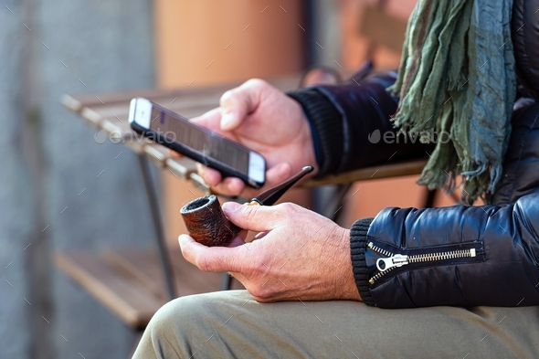smoking pipe and smartphone in male hands, close-up