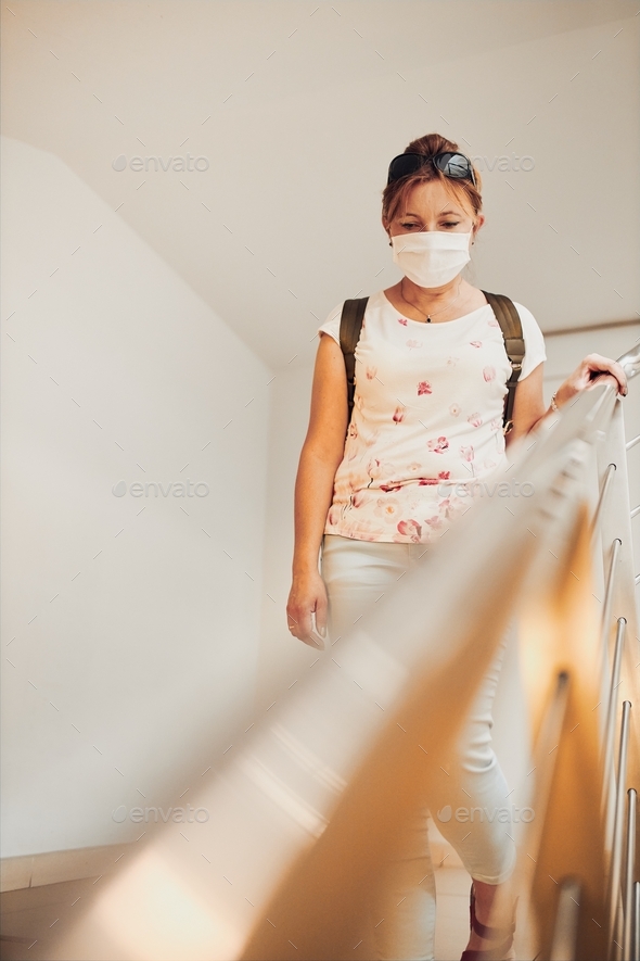 Woman going downstairs in public place inside wearing face mask to cover mouth and nose