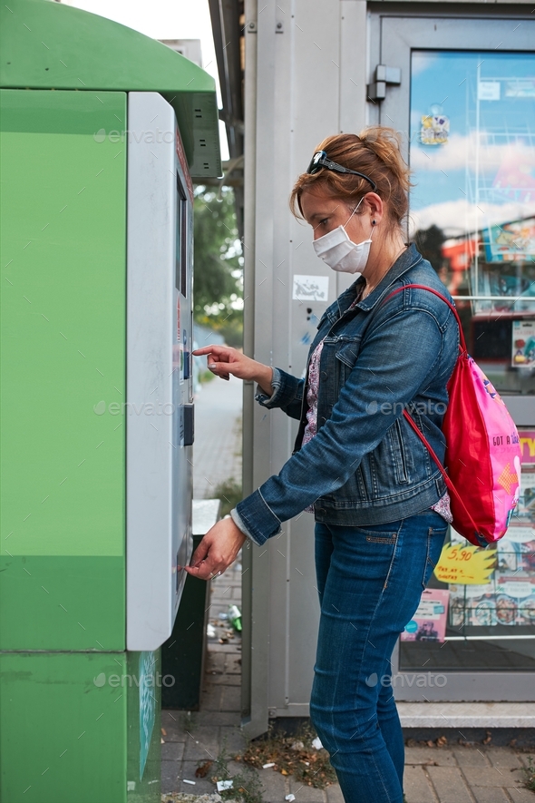 Woman buying bus ticket in ticket machine wearing face mask to cover mouth and nose