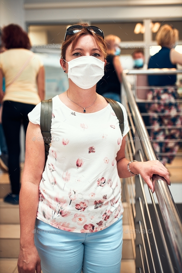 Woman going downstairs in public place inside wearing face mask to cover mouth and nose